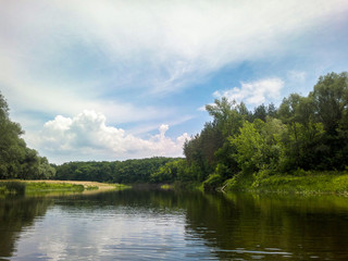 Summer landscape by the river. Beautiful green shores and a quiet river. Peaceful nature in summer.