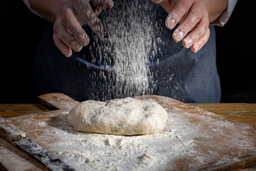 Female hands knead the dough on a wooden antique table on a dark background, close-up, shallow...