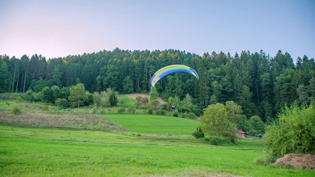 Slow motion shot of a professional para glider landing on a green hill in Slovenia