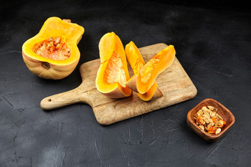 Butternut squash pieces, wooden bowl with pumpkin seeds, cutting board on black background,...