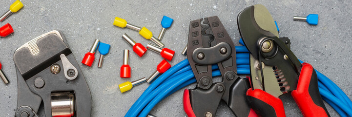 Tools and tips of various sizes and colors for crimping stranded electrical wires. Crimping tools, wire tips and electrical cable on a gray concrete background. Banner