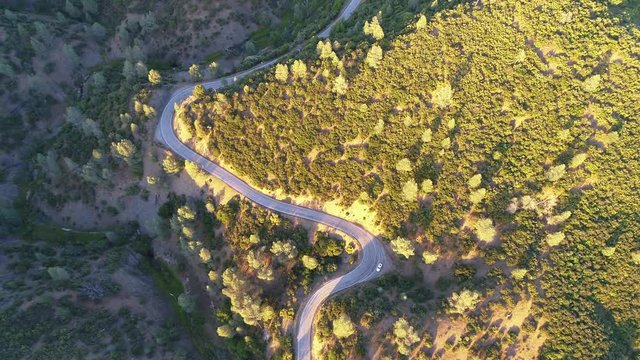 Winding road on the edge of a mountain. Aerial view in daylight with green trees and white Nissan GTR parked car off the two-lane highway.