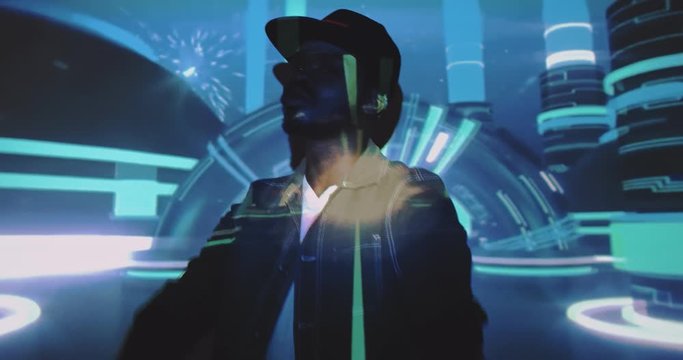 Young stylish African American man in cap dancing and moving at camera with blue graphic projections on him. Art digital concept videoshooting. Male model or dancer with projected futuristic figures.