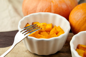 Baked pumpkin piece on fork, vegatables, white ceramic bowl on blurred background
