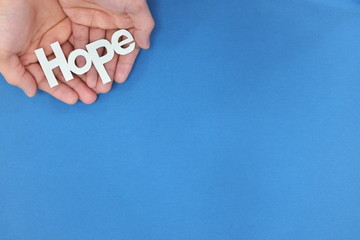 Human hands holding hope word cutout. Top view, blue background with copy space.
