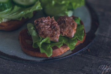 sandwiches with toasted bread, pork, herbs, iceberg lettuce on a wooden tabletop. dark photo with selective focus
