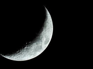 increasing sickle-shaped quarter moon with its moon craters stands in the black night sky