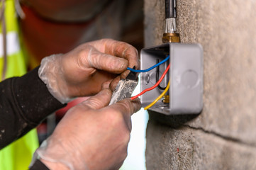 Male electrician cutting wire for socket plug on garage wall