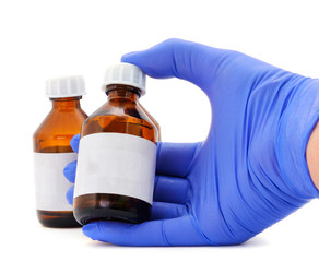 Female hand in blue latex medical glove holds a brown glass bottle for medicines.