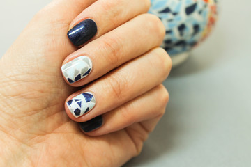 Short natural nails are covered with gel Polish with a geometric design on the hands of a fashionable girl