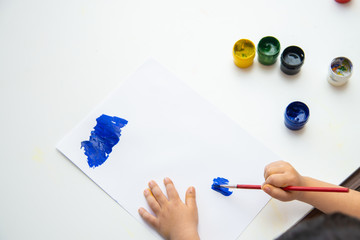 Little boy hand draws on paper. Cute Child boy is sitting and painting. Stay home