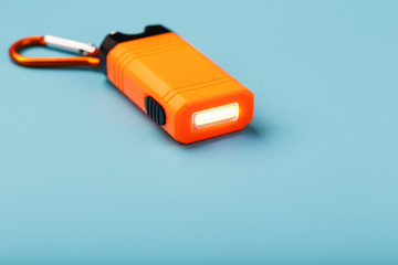 Orange led Flashlight with a carabiner on a blue background. LED lights in flight.