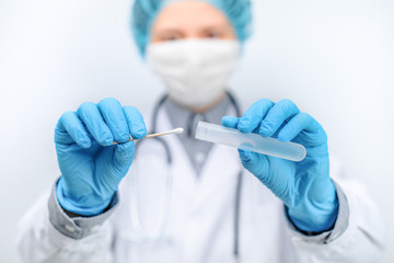Arzt vor weißem Hintergrund hält ein Abstrich Röhrchen in den Händen für eine Testung um auf Bakterien und Viren. Mediziner hat eine Probe entnommen um auf Krankheitserreger zu untersuchen. - obrazy, fototapety, plakaty