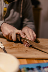 A man cuts a traditional French dried sausage or saucisson on a wooden plank