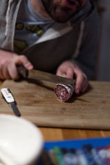 A man cuts a traditional French dried sausage or saucisson on a wooden plank