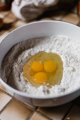 A mixing bowl is filled with plain white flour and three eggs