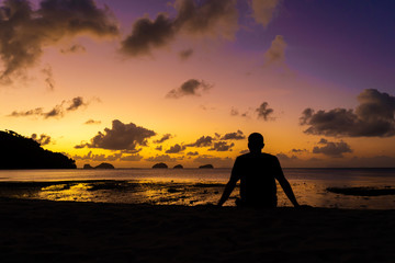 A guy silhouette enjoys a beautiful beautiful sunset on a tropical beach. Fiery sunset on the ocean