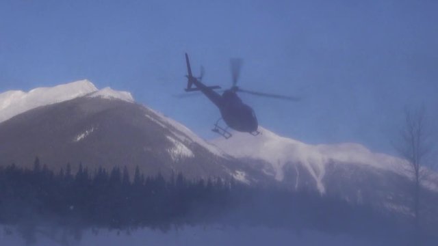 Red helicopter creates snow cloud as it lifts off in winter Rockies