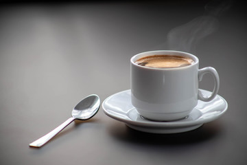Obraz na płótnie Canvas A cup of hot coffee on a gray background with a spoon on the table. Good morning.