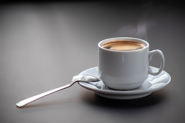 A cup of hot coffee on a gray background with a spoon on the table. Good morning.