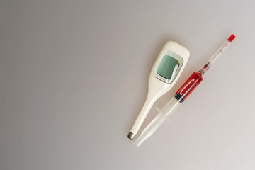 syringe filled with red liquid and electronic thermometer on a light background