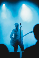 Silhouette of a man playing the guitar on stage. Dark background, smoke, spotlights