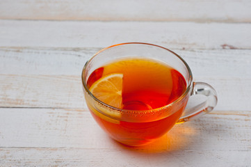 Glass cup with tea and lemon standing on a white painted wooden surface. Background for hot drinks. Soft and tonic drinks.