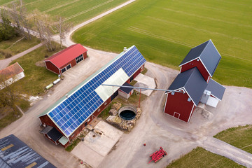 Top view of rural landscape on sunny spring day. Farm with solar photo voltaic panels system on wooden building, barn or house roof. Green field copy space background. Renewable energy production. © bilanol