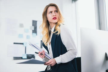 young woman manager holding documents in her hands, looks busy while studying business contracts, multitasking, work concept