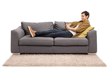 Young man resting on a sofa and looking at a mobile phone