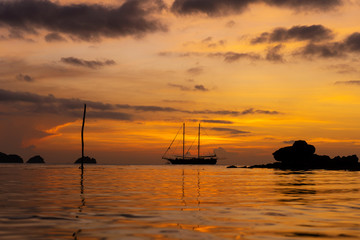 Colorful sunset on a tropical beach. Orange sunset on the ocean. Colorful sunset in the tropics. In the water is a sailing ship. Silhouetted sailboat with masts