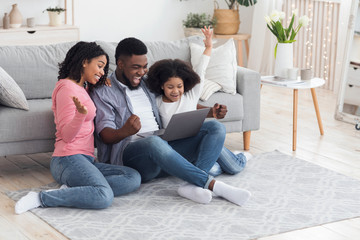 African mother, father and daughter celebrating success with laptop at home