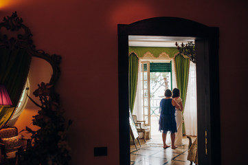 Fototapeta premium mom and bride stand with their backs in the hotel room, mom helps the bride to fasten the wedding dress