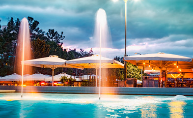 terraces with umbrellas near the fountain at dusk