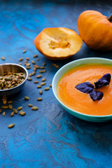 Pumpkin soup with purple Basil on a blue background with crispy toasted pumpkin seeds.