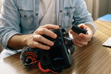 A photographer or videographer changing the battery of his camera. The camera has an external microphone for vlogs and videos on social networks