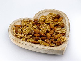 Mix of different nuts on the plate: almond, hazelnut, walnut in a heart form on the white background