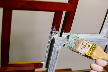 the master paints with a brush a wooden brown photo frame with light paint
