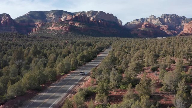AERIAL: Shot in Sedona Arizona of a car driving through rock formations and a beautiful landscape on a sunny day