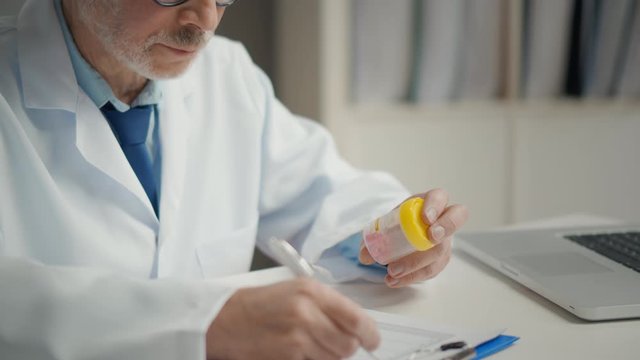 Close portrait of Elderly doctor examining medicine and writing notes