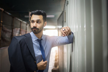 Young south asian businessman wearing suit leaning on metal wall inside the underpass to take a break on his way to work.