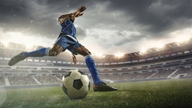 Professional football or soccer player in action on stadium with flashlights, kicking ball for winning goal, wide angle. Concept of sport, competition, motion, overcoming. Field presence effect.