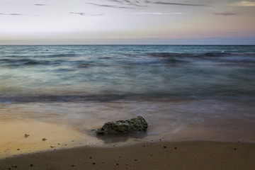 roca en la arena frente al mar al atardecer