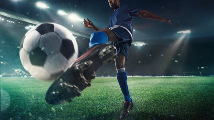 Professional football or soccer player in action on stadium with flashlights, kicking ball for winning goal, wide angle. Concept of sport, competition, motion, overcoming. Field presence effect.