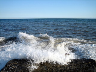 A splash of sea water on a stone pier with lots of foam and spray on a Sunny day against a flat horizon.