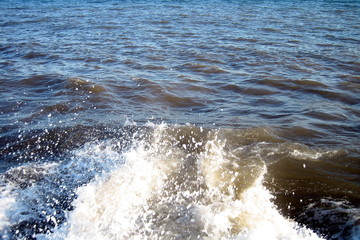 A splash of sea water on a stone pier with lots of foam and spray on a Sunny day against a flat horizon.