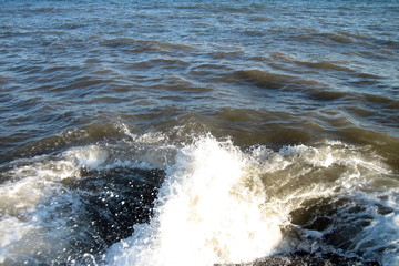 A splash of sea water on a stone pier with lots of foam and spray on a Sunny day against a flat horizon.