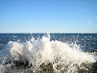 A splash of sea water on a stone pier with lots of foam and spray on a Sunny day against a flat horizon.