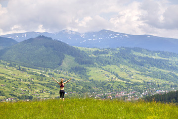 Fototapeta na wymiar Slim young woman with raised arms outdoors on background of beautiful mountain landscape on sunny summer day.