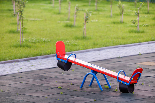 Seesaw swing in big yard with soft rubber flooring on sunny summer day.